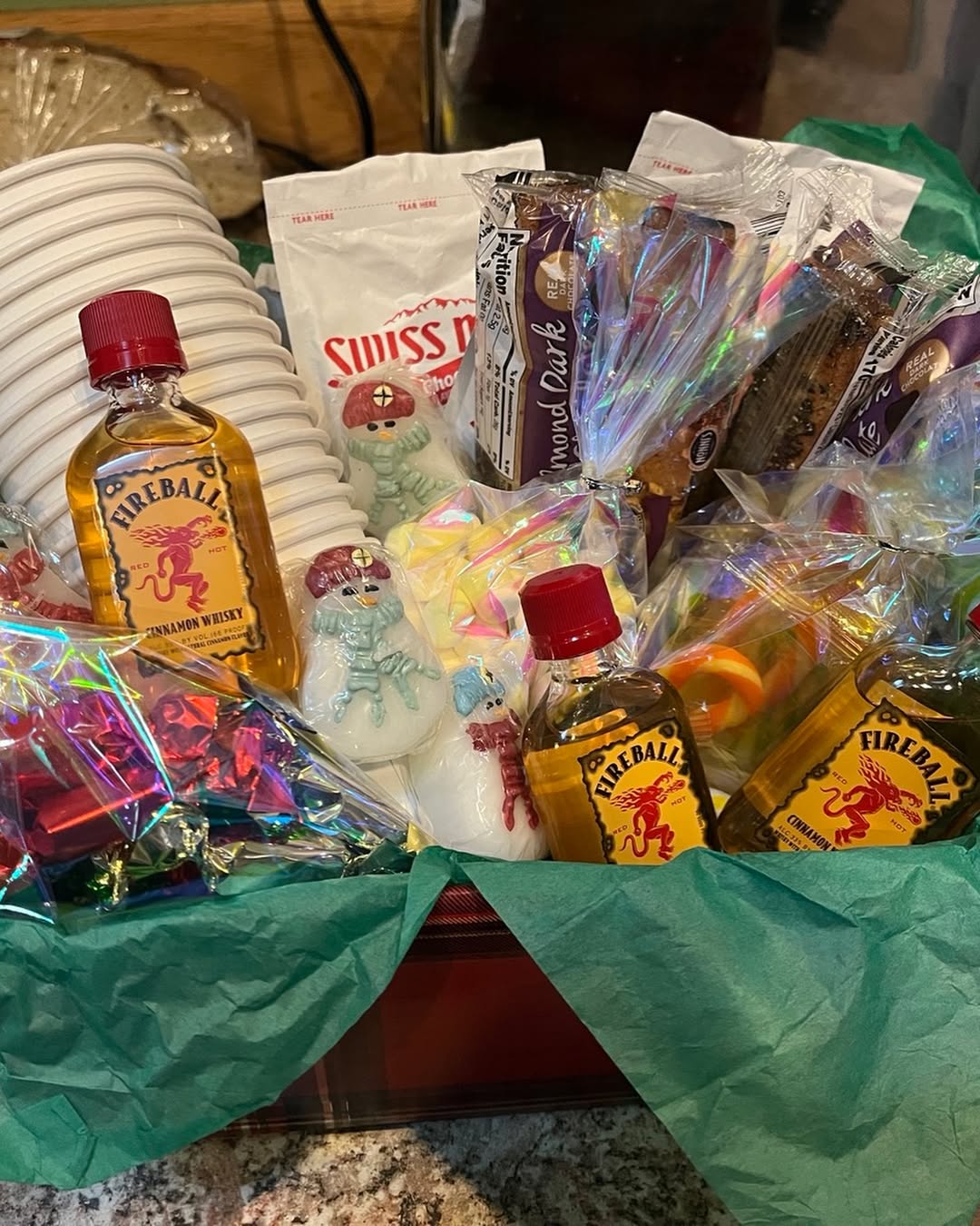 A festive hot cocoa basket with Fireball whisky, Swiss Miss packets, mugs, and sweet treats