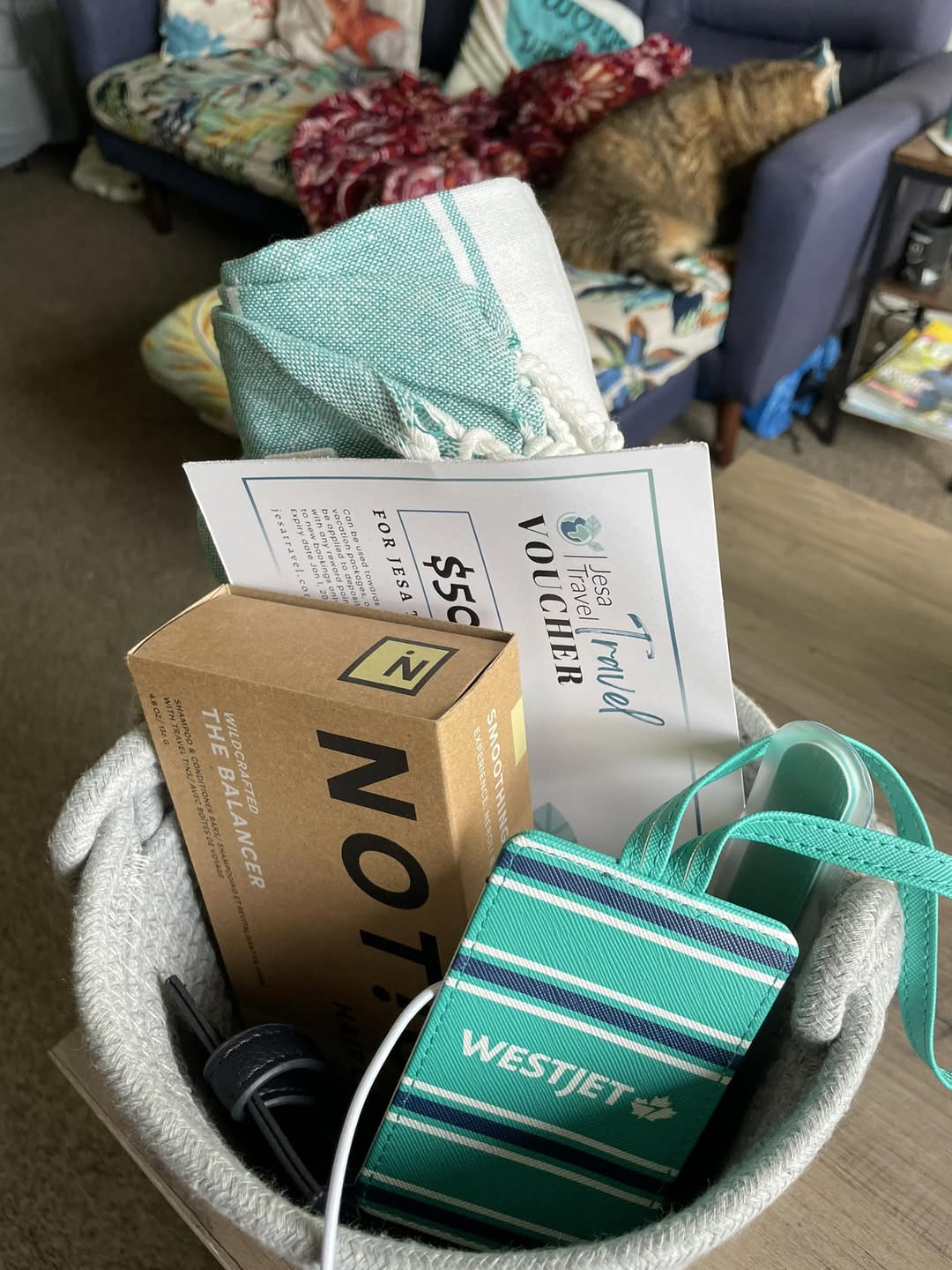 A travel gift basket with a voucher, luggage tag, towel, and handy travel essentials