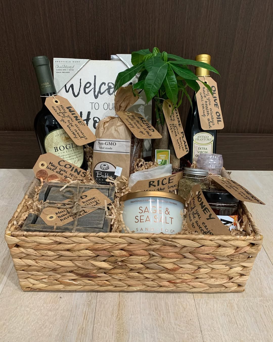 A housewarming gift basket with wine, olive oil, rice, a plant, and thoughtful labeled items