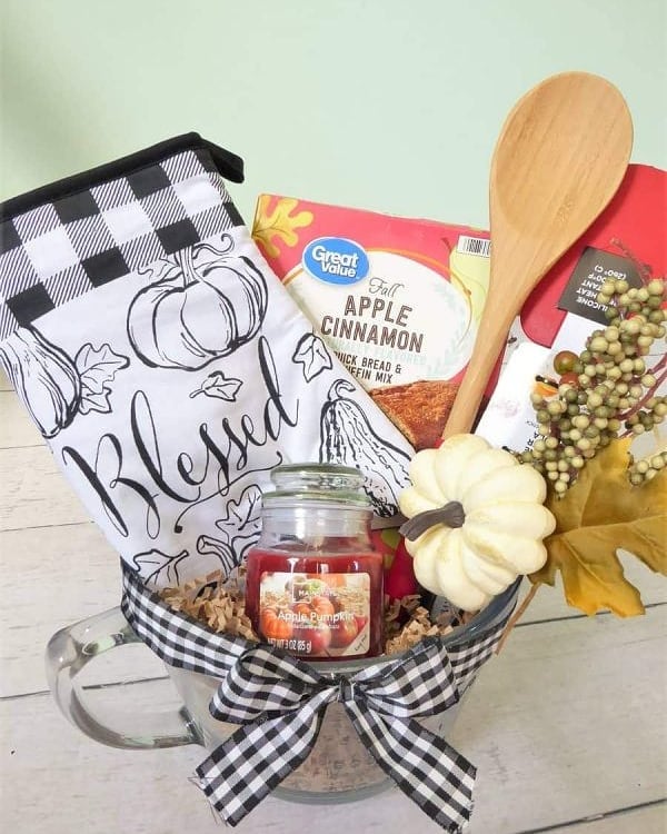 A fall-themed baking basket with apple cinnamon mix, a kitchen towel, candle, and wooden spoon